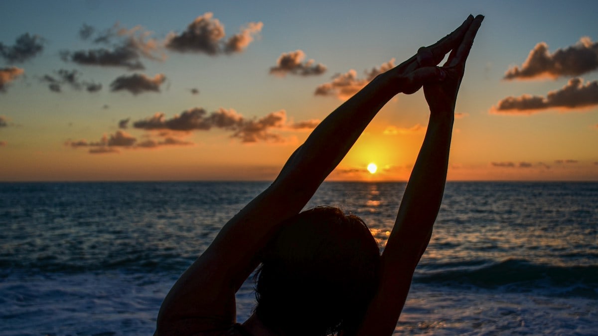 silhouette of woman raising her hands on beach during sunset